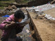 A child drinks water near a stream in Fuyuan county