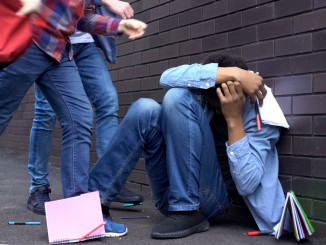Cruel teenagers scattering classbooks of afro-american boy, school bullying